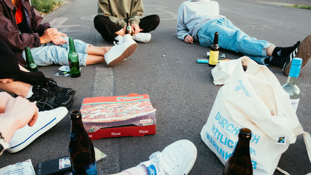 Teenager sitzen auf Straße im Kreis mit Alkohol und Pizza